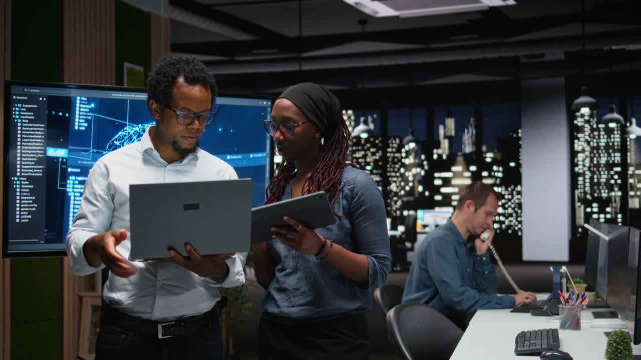 Diverse Business Team Collaborating on Laptop and Tablet in Modern Office at Night