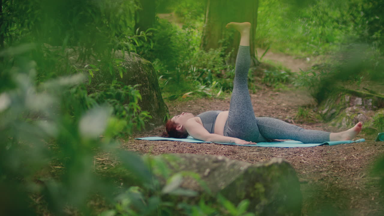 Pige der dyrker yoga i en skov, totalbillede, glidende skud med blade.