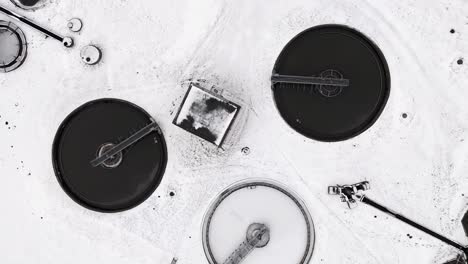 Circular-machines-in-snow-covered-water-treatment-plant,-aerial-drone-view-from-left-to-right