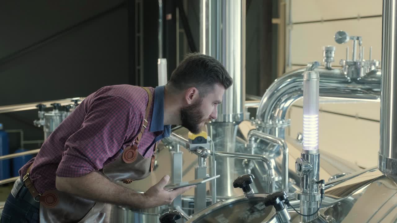 un joven cervecero con un delantal de cuero supervisa el proceso de fermentación de la cerveza en una fábrica de cerveza moderna