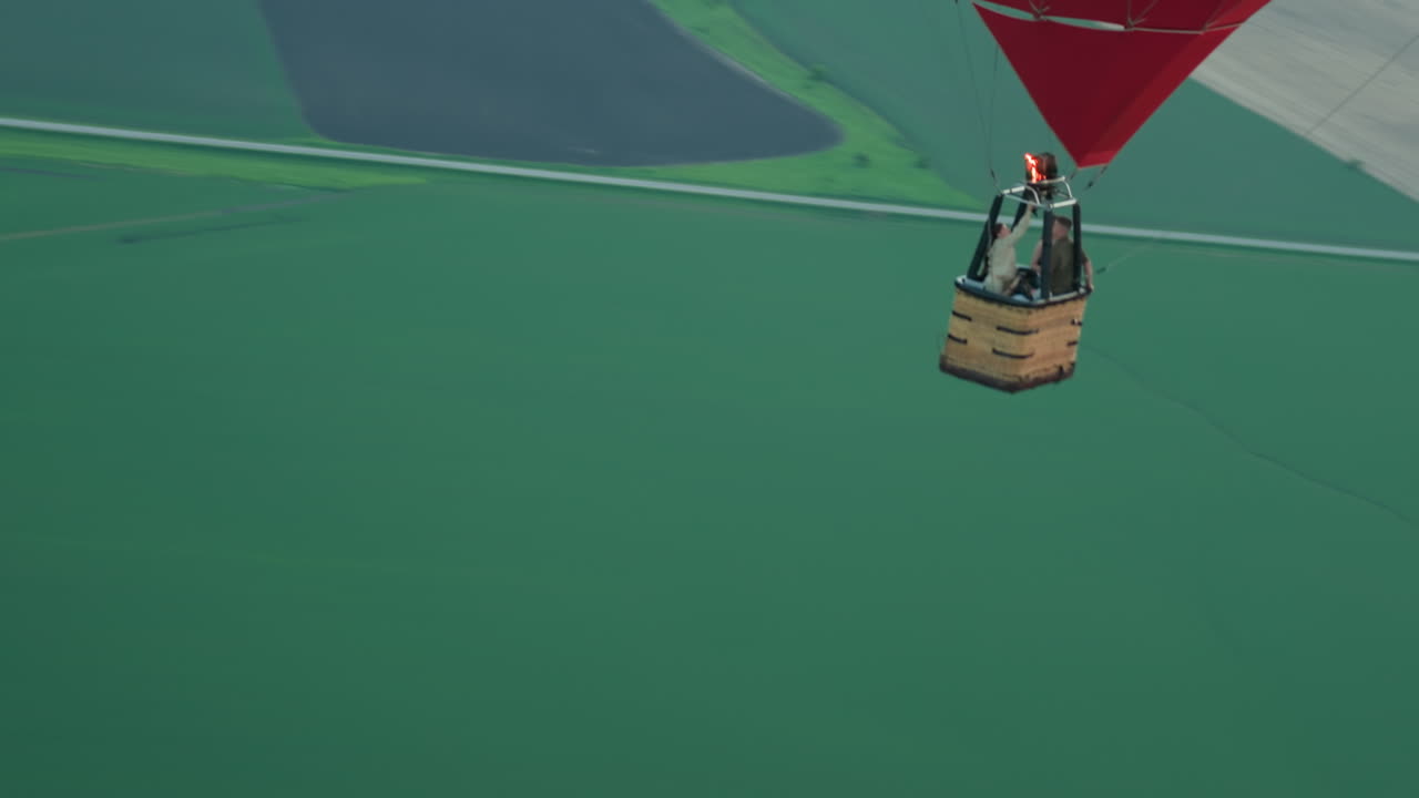 close up of colorful hot air balloon basket holding passengers as pilot ignites burner to lift balloon over green field under soft evening sky with flame jet upward capturing aerial adventure scene