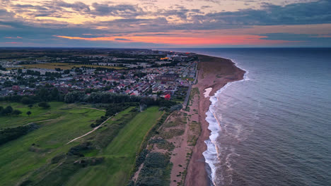 Drone-footage-showcases-Skegness-coastal-town-at-sunset,-including-holiday-park,-beach,-caravans,-and-sea