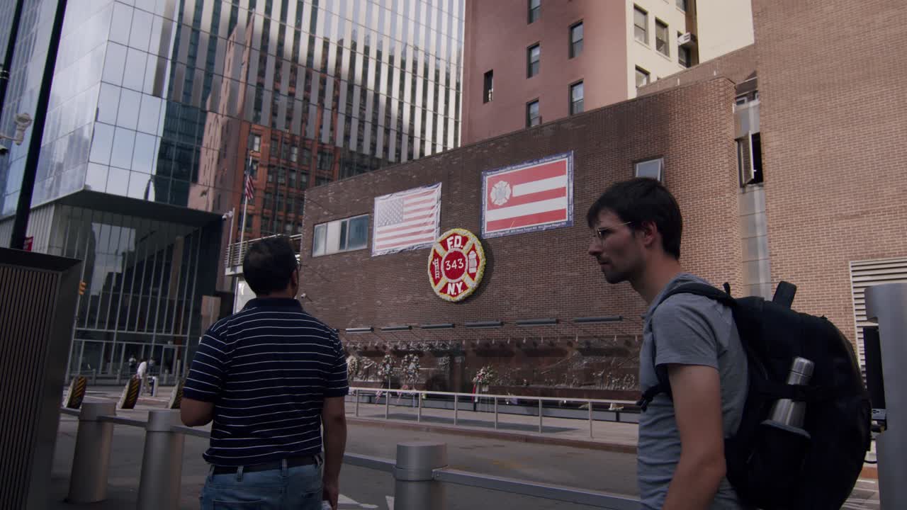 Tourists visiting the 9 11 Memorial near a New York Fire Department tribute wall on a sunny day