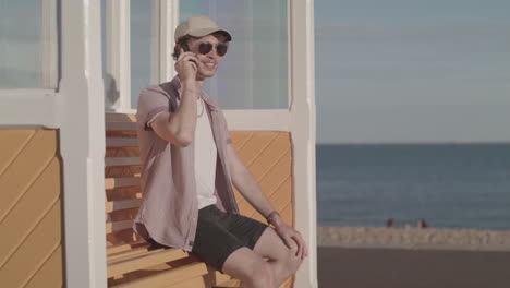 a man sat on a bench on the beach receives a call from a good friend