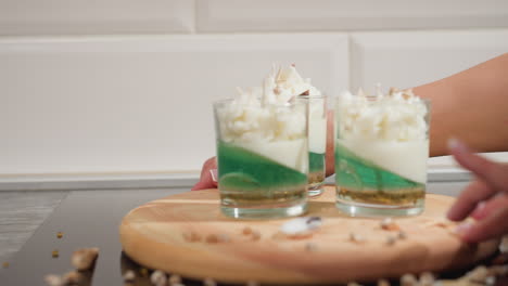 baker carefully rotates wooden tray counterclockwise displaying realistic cupcake candles in layered glass cups topped with whipped designs, surrounded by scattered decorative toppings