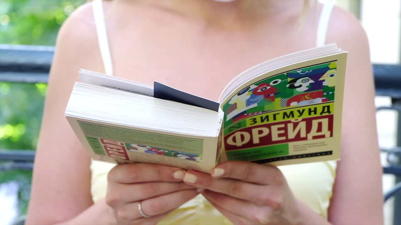 Chisinau, Moldova - August 18, 2021: Woman wearing a mask, reading Group Psychology and the Analysis of the Ego book by Sigmund Freud in Russian, at a terrace