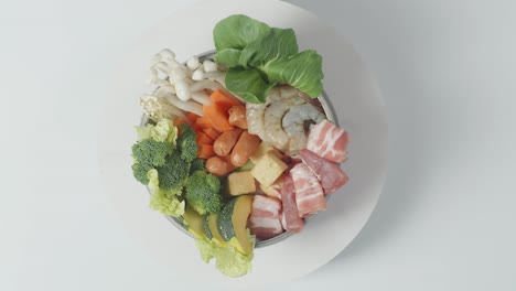 cerca de una olla de ingredientes de shabu girando alrededor de la mesa blanca en la cocina