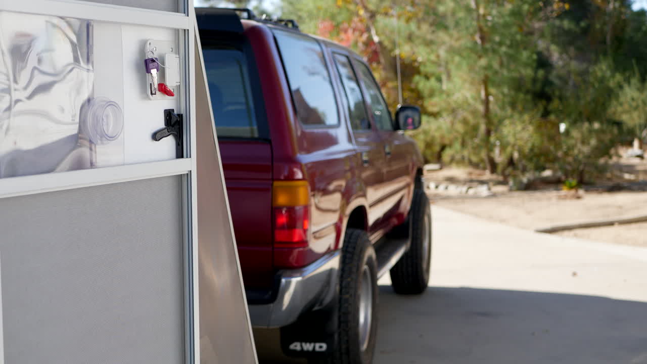 캘리포니아의 캠프장 여행에서 맞춤형 금속 눈물방울 여행 트레일러와 빨간색 suv 견인 차량의 측면을 따라 왼쪽으로 미끄러집니다.