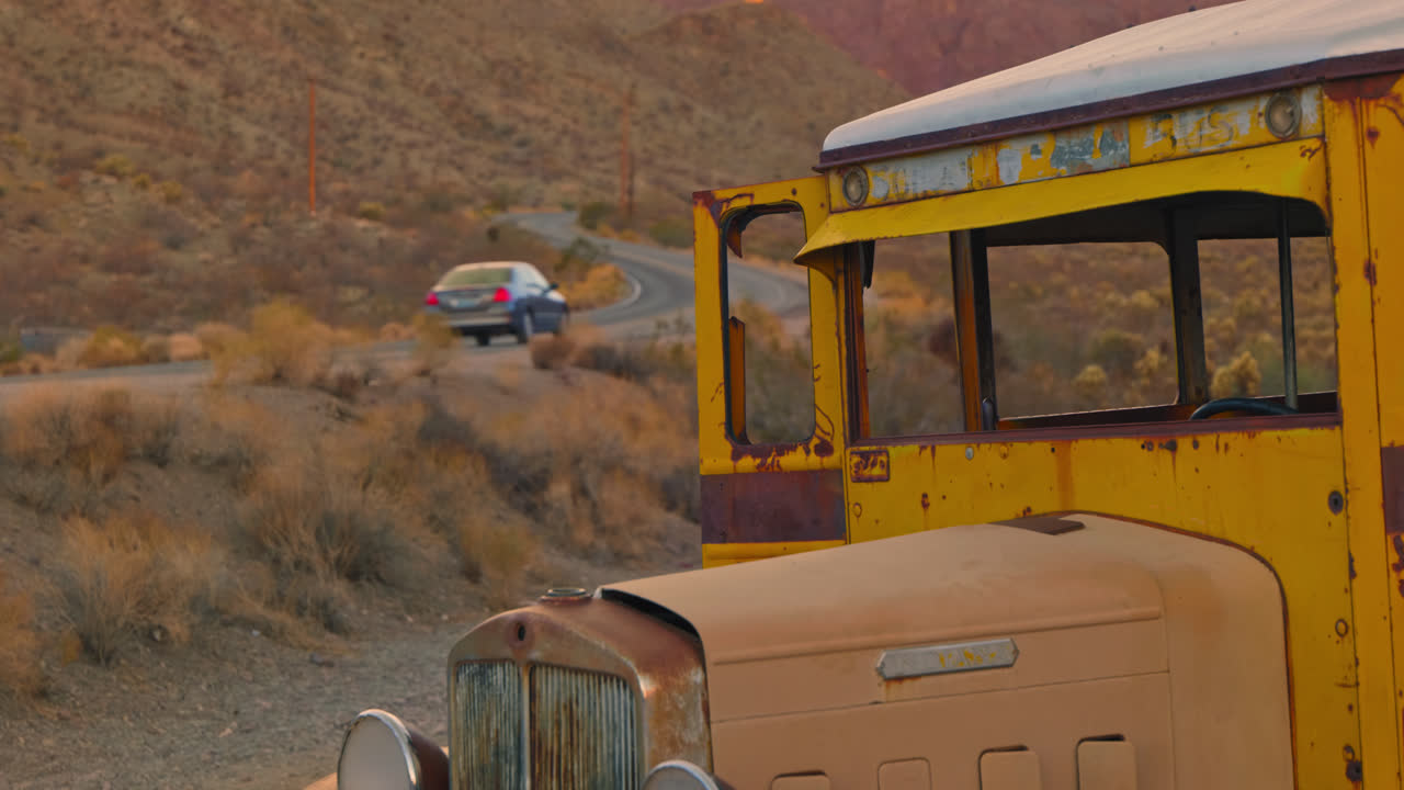 A car drives past an old abandoned school bus sitting on the side of the road.