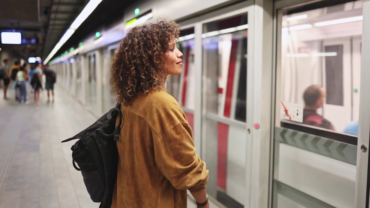 Giovane donna con capelli ricci che aspetta il treno della metropolitana sulla banchina