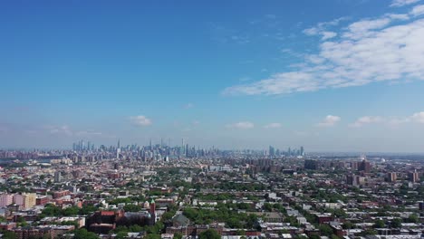 an aerial view over bedford stuyvesant, brooklyn in ny. it is a sunny and clear day. the drone camera pans left to show the manhattan skyline on the horizon in the distance.