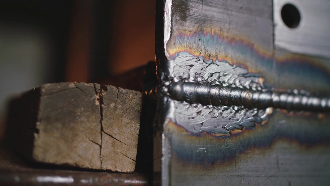 Mostrando el cordón de soldadura de una placa de acero vertical enfriándose después de soldar en un banco de trabajo de metal con un bloque de madera.