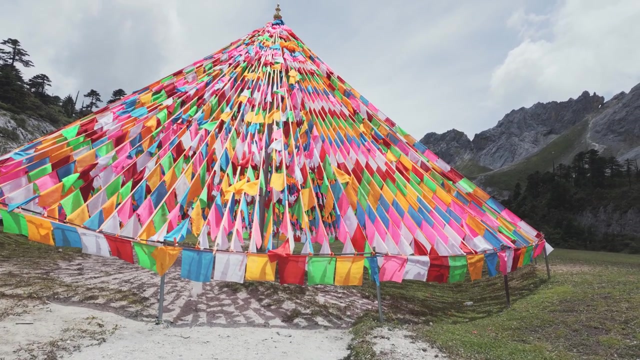 Autentiske tibetanske bedeflag arrangeret i en pyramideform vajer i vinden mod en baggrund af barske bjerge. Nyttigt til rejsedokumentarer og indhold om kulturel velvære.