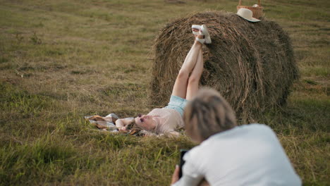 photographer capturing back view shot of model posing with legs up on hay bale in rural setting, golden field, picnic basket, and natural light create serene countryside