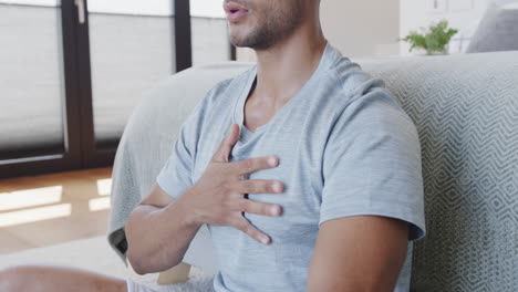 hombre biracial relajado sentado en el suelo en casa practicando yoga meditación y respiración, cámara lenta