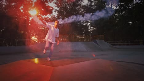 un joven está sosteniendo una llamarada de señal roja brillante mientras realiza un breakdance en la pista de la bomba del rollerdrome por la noche.