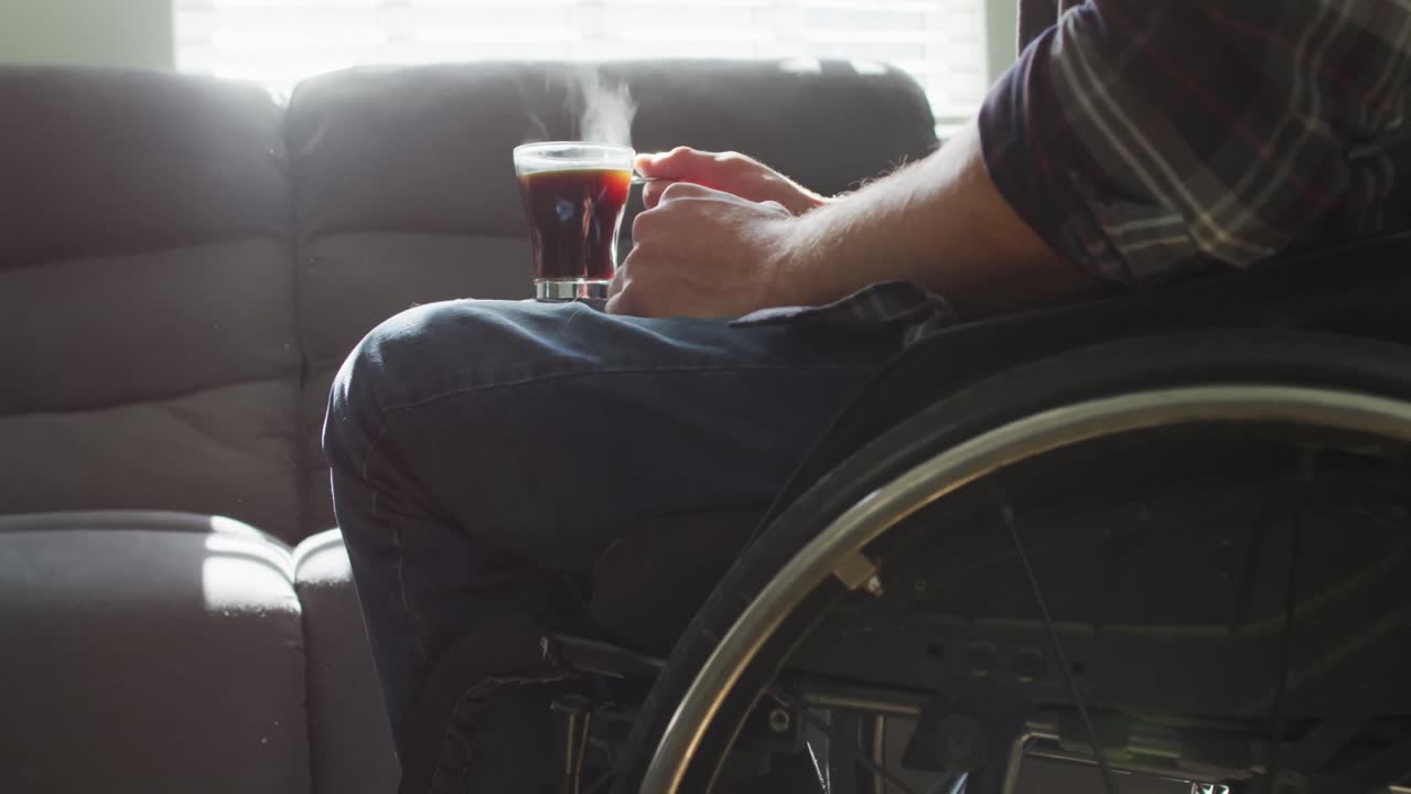 sección media de un hombre discapacitado caucásico en silla de ruedas sosteniendo una taza de café en la sala de estar