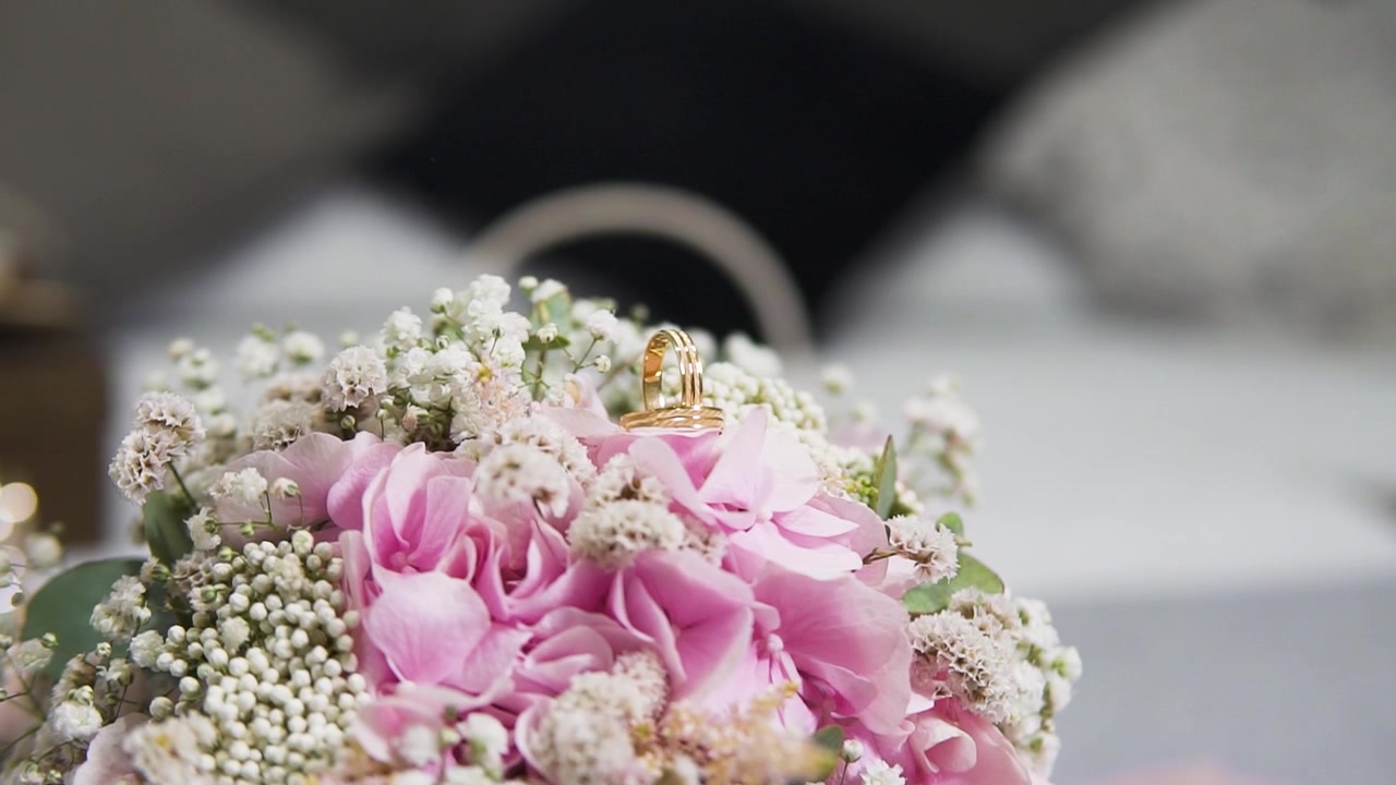 Cirkulær optagelse af guldringe placeret ovenpå lyserøde og hvide blomster på bryllupsdagen