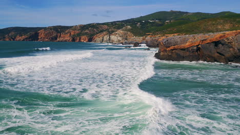 aerial view sea waves barreling to rocky shoreline with white foam slow motion