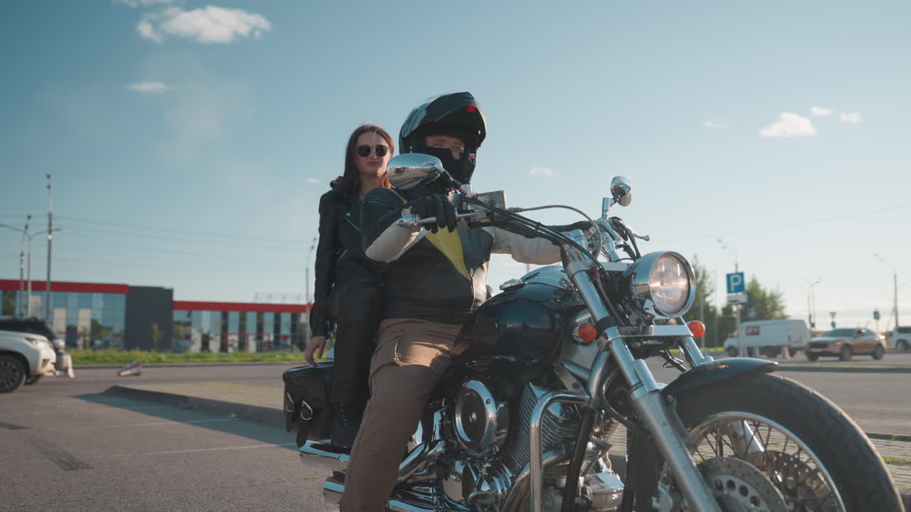 Elegant woman in black leather climbs motorcycle holding rider dressed in helmet and jacket, urban street background with sunlight and chrome details highlighting biker lifestyle