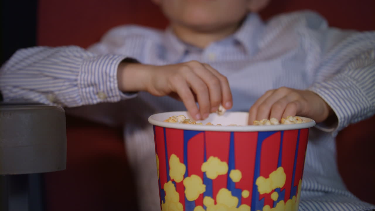 las manos de los niños tomando palomitas de maíz de la caja de papel. comida de cine para niños