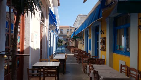 Mesas-Vacías-Para-Comer-Fuera-De-Un-Edificio-Blanco-Con-Colores-Azul-Y-Amarillo-En-Preveza,-Grecia