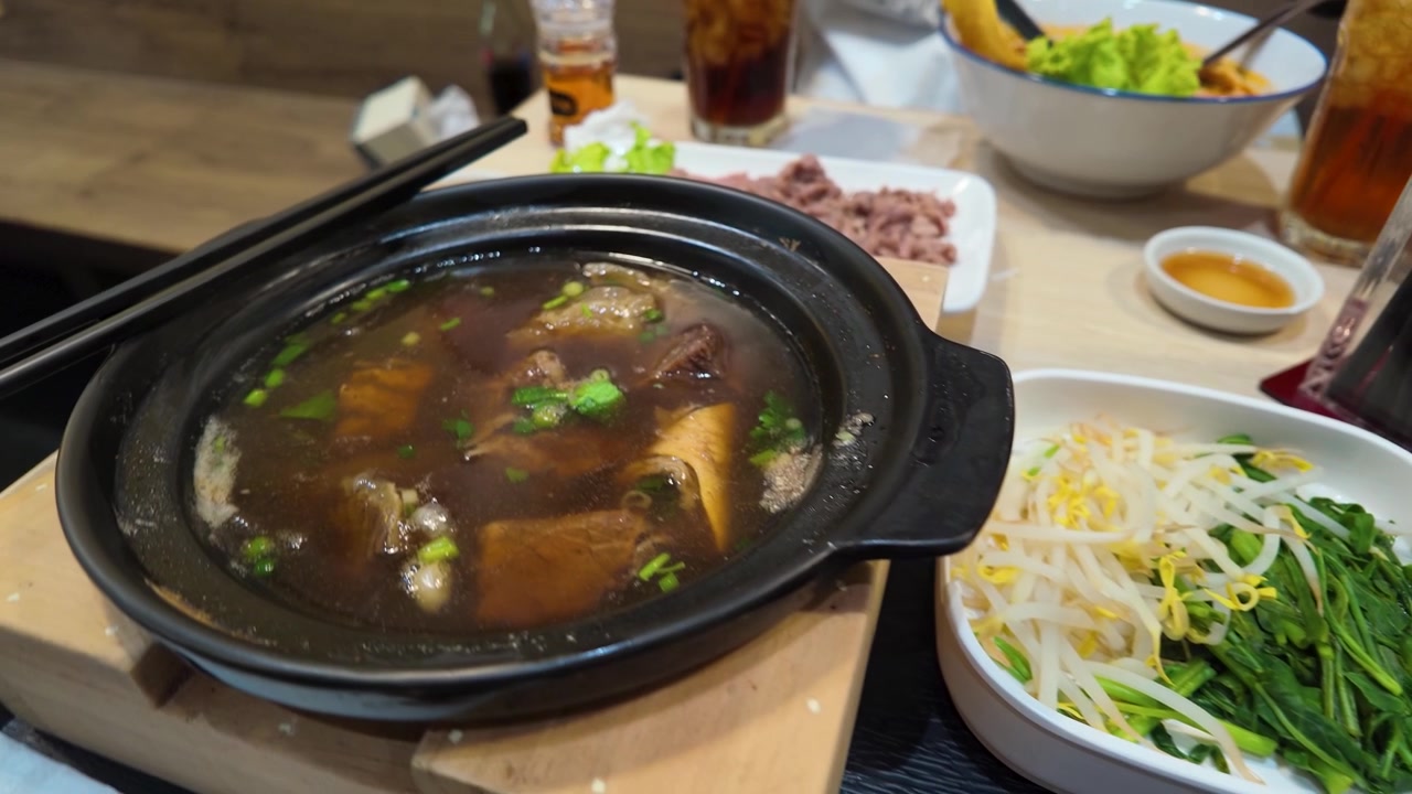 Tampilan dekat sup mi daging sapi Thailand tradisional, irisan daging, dan es teh di Bangkok.