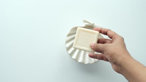 la mano recogiendo una barra de jabón de un plato de jabón con conchas marinas