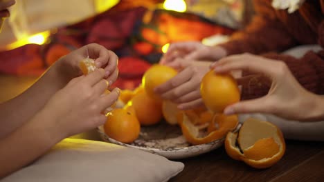 Close-up-of-hands,-family-having-good-times,-eating-mandarines-under-Christmas-tree-in-lights