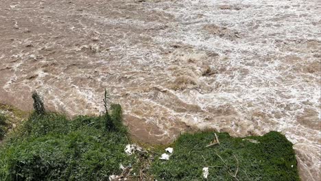 Brown-water-flows-at-Rimac-River-in-Lima,-Perú-near-garbage-and-green-grass