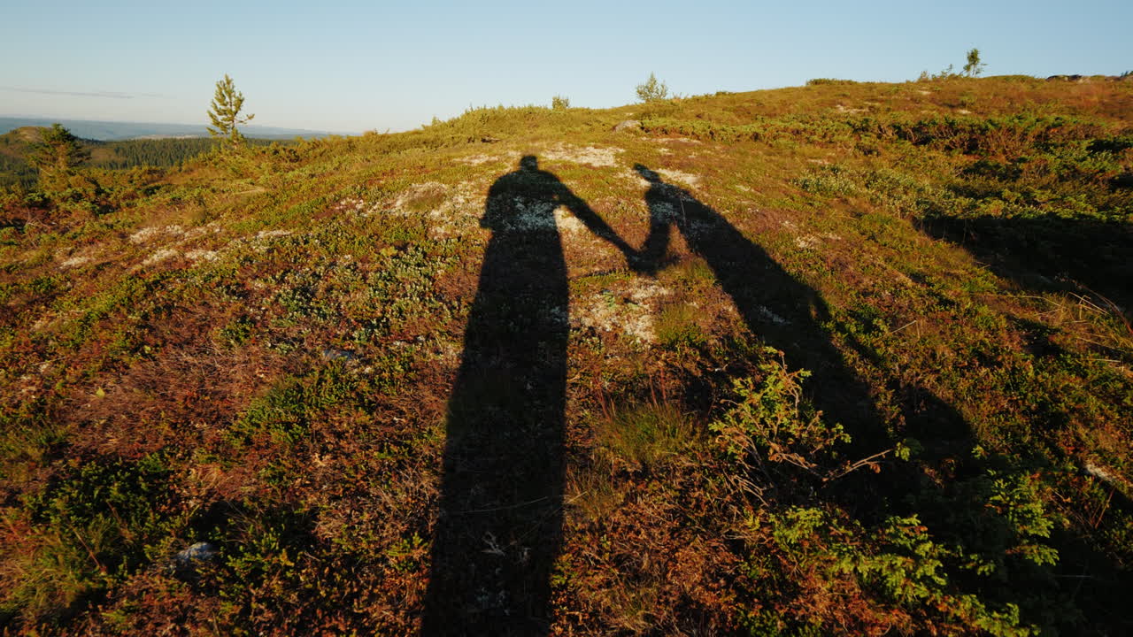 las sombras de dos viajeros caminan por el terreno montañoso tomados de la mano estilo de vida activo