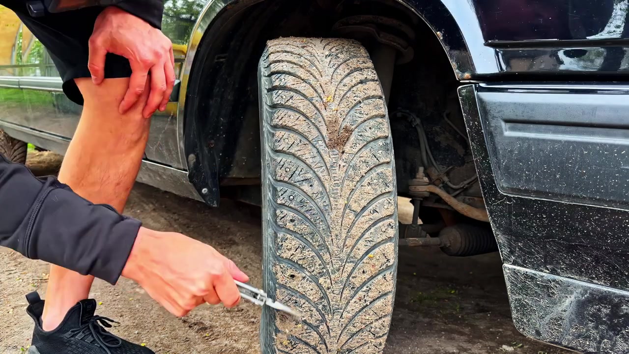 Close-up of a person using pliers to remove debris from a dirty car tire tread, showing practical vehicle maintenance and roadside safety inspection.