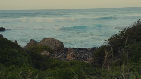 rolling-turquoise-waves-of-the-Pacific-Ocean-crash-onto-the-rocky-Hawaiian-shore-at-Kaena-Point-Oahu-shot-through-a-gully-in-the-cliff