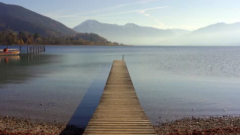 long jetty pier in placid lake with background mountains in autumn