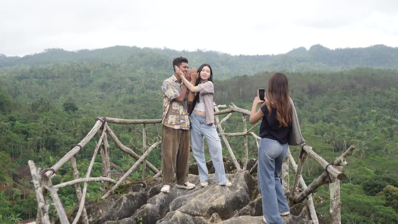 เพื่อนชาวเอเชียอินโดนีเซียวัยหนุ่มสาวกำลังถ่ายรูปด้วยโทรศัพท์ที่จุดชมวิวภูเขาในการท่องเที่ยวธรรมชาติ