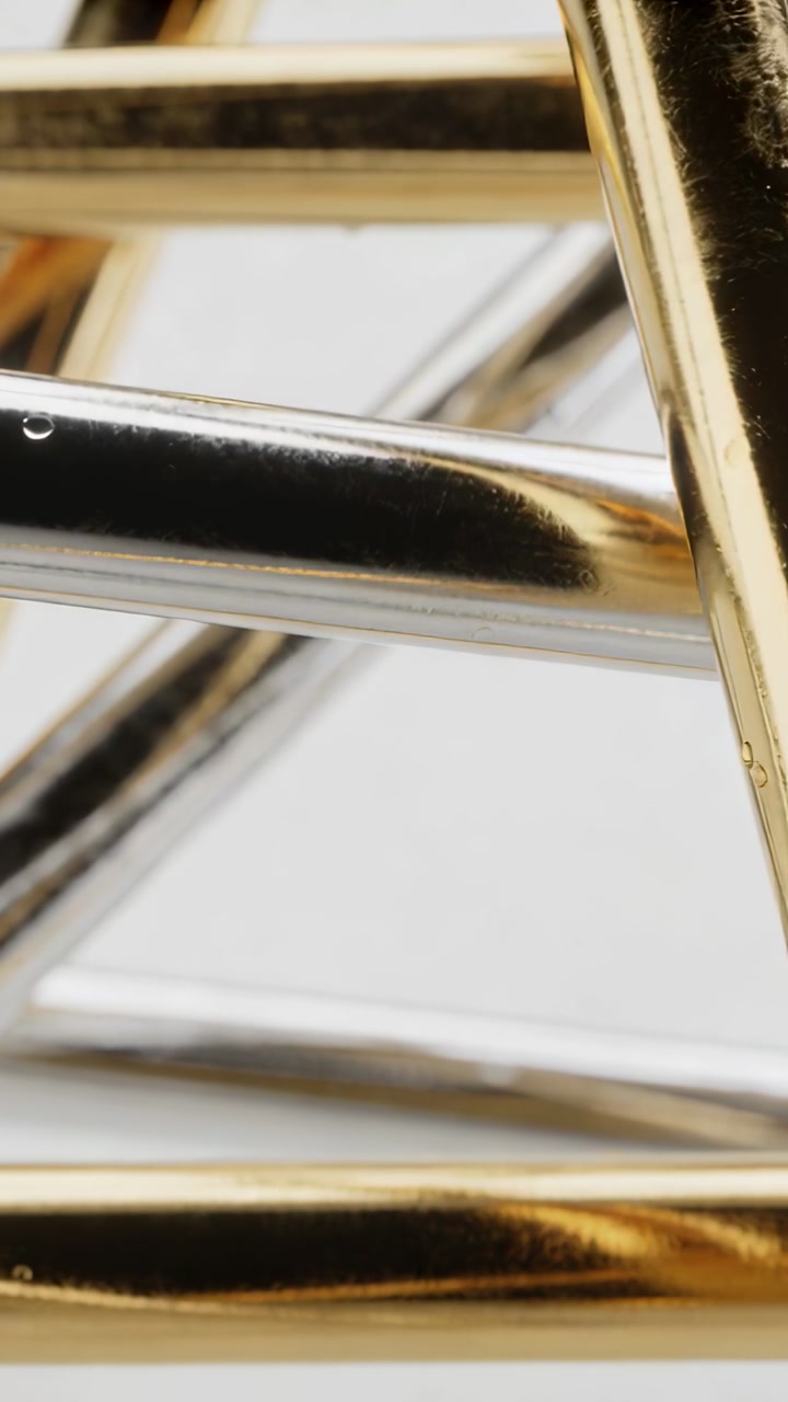 Vertical video: Shifting camera studying gold, silver intersecting tubes at studio, droplet visible