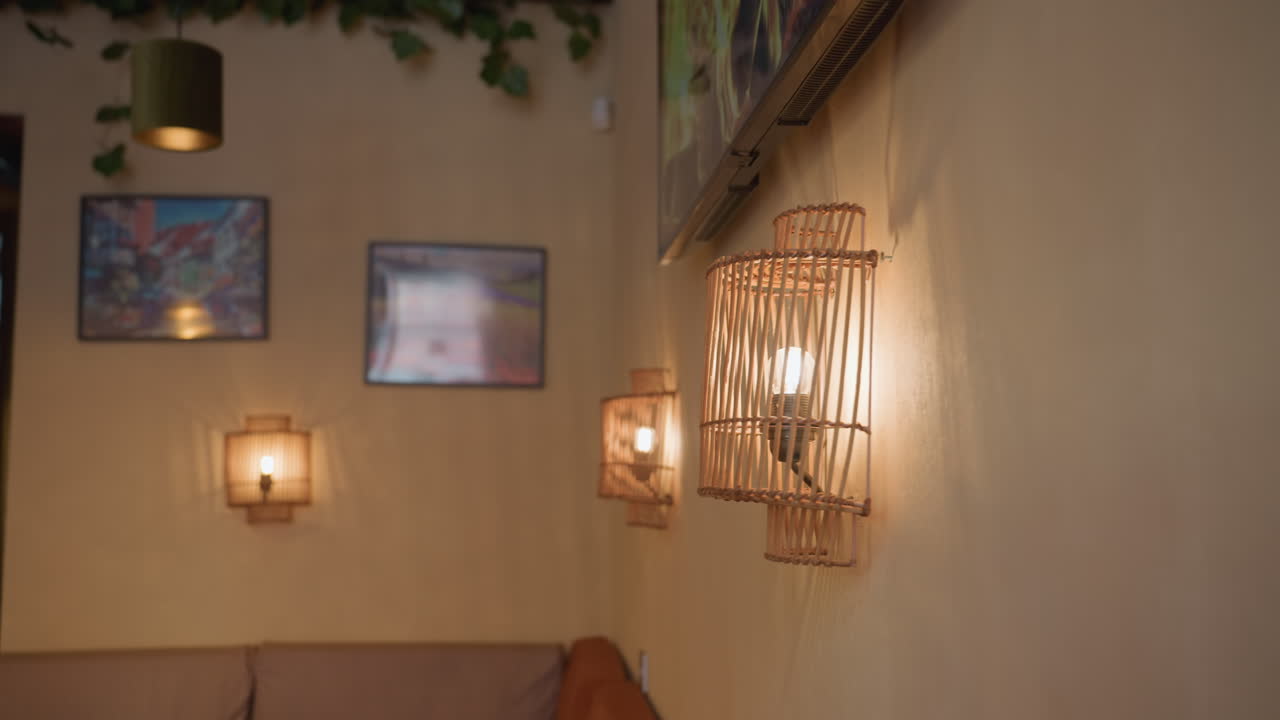 Close up of glowing light bulb enclosed in vertical wooden decorative frame on softly lit wall with blurred background showing additional lamps and television