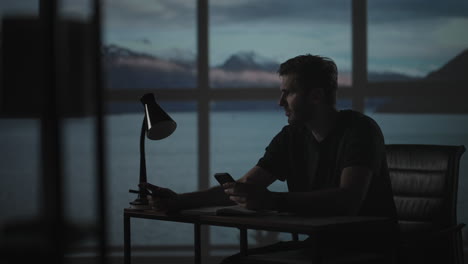 a thoughtful man sitting at a table with a desk lamp writes with a pen. dark time of the day twilight on the background of the window a sad man thinks and writes