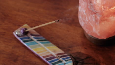 bursting smoke incense on a multicolored holder besides a pink salt lamp over a wooden table