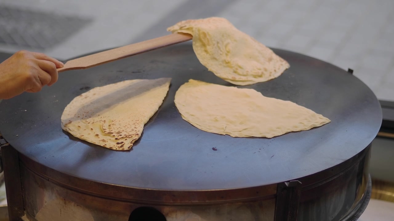 Venditore ambulante che cucina pane piatto tradizionale su una grande piastra