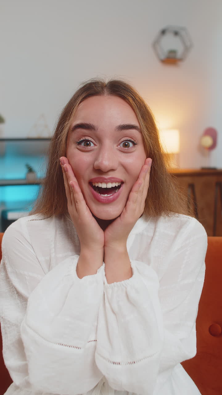 Young woman surprised looking at camera with big eyes shocked by sudden victory celebrating at home