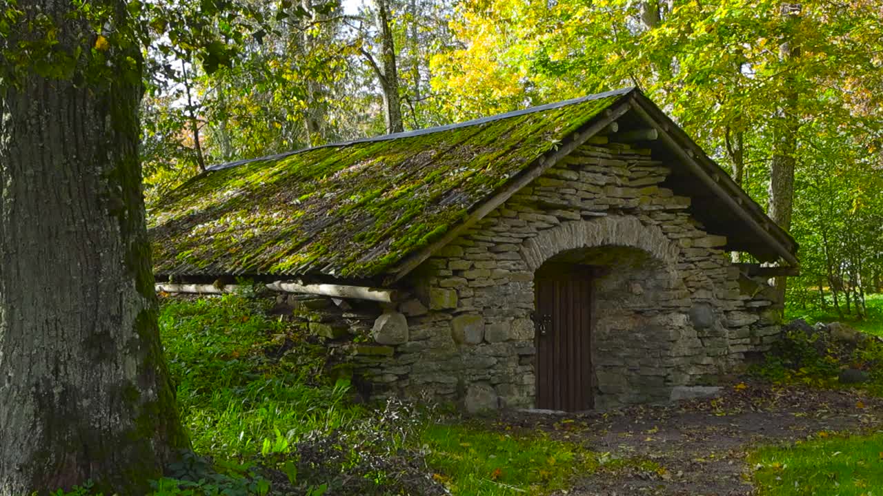 Gorgeous old limestone building or a cellar in sunny forest during autumn or summer time in Saku mansion park with stone roofing that is covered with green moss. Building has a wooden brown door.