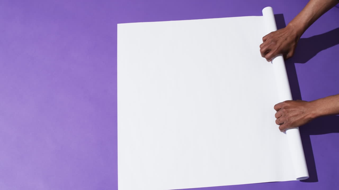 Video of hands of african american man with rolling up white paper on paper background