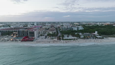 Aerial-drone-dolly-in-view-of-a-cityscape-by-the-coast,-with-built-structures,-rolling-clouds-and-endless-horizon-in-Playa-del-Carmen,-Mexico