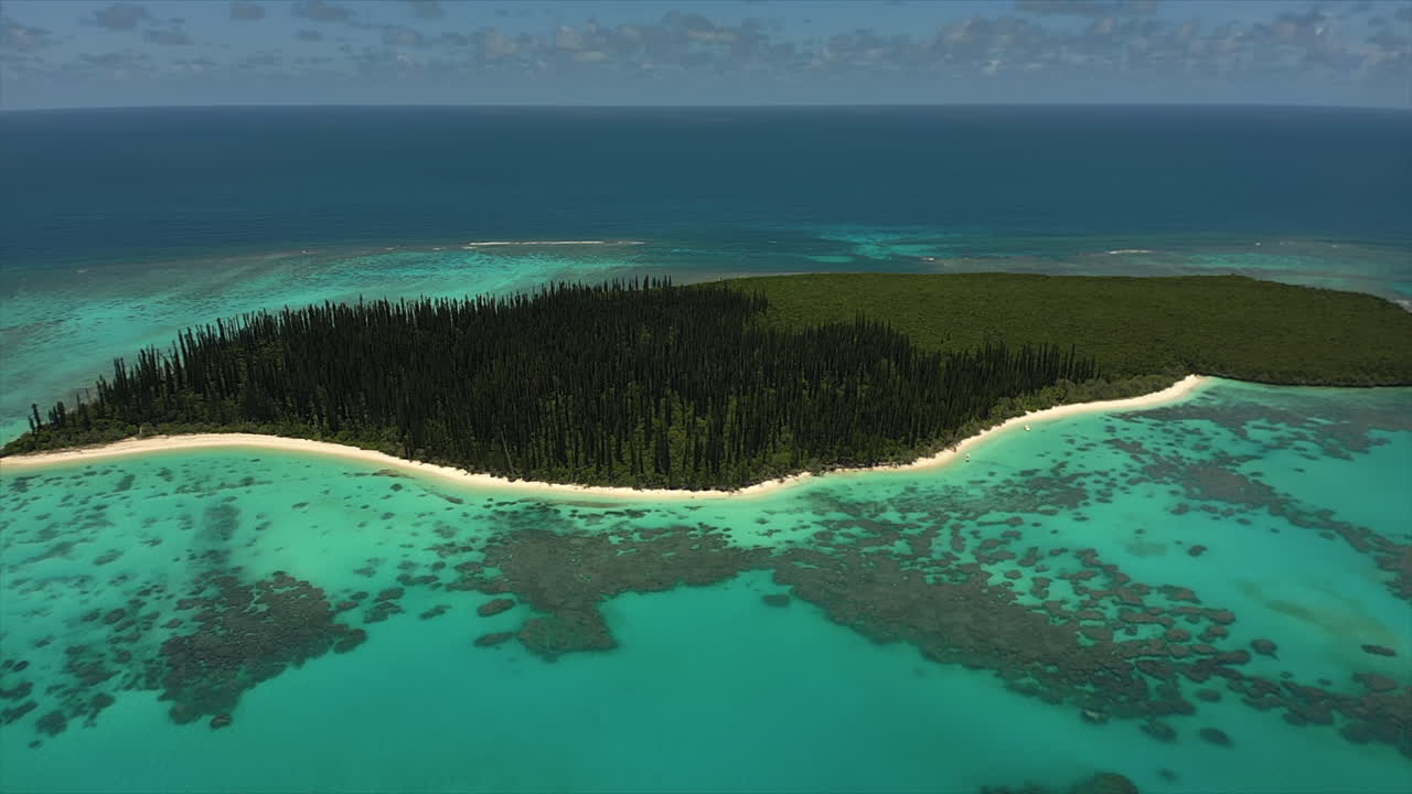 Den øde Ilot Brosse, eller Brush Island, i Isle of Pines, halvt dækket af skov af ikoniske søjleformede fyrretræer fra luften, langsom rotation mod uret