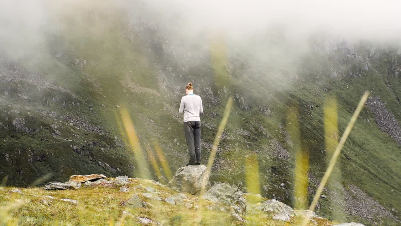 카메라 : 절벽 가장자리에 있는 작은 바위 위에 서서 구름이 가득한 산의 풍경을 즐기고 사진을 찍는 남자