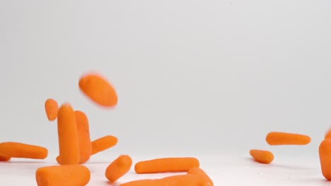 bright orange baby carrots raining down onto white table top and bouncing in all directions in slow motion