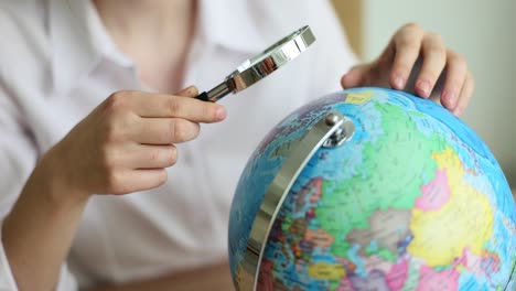 person examines a globe with a magnifying glass