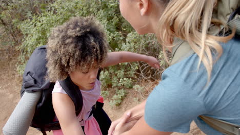 a young child with curly hair receives help from a woman outdoors