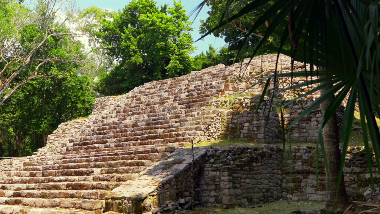 Antiche rovine Maya a Oxtankah, Messico. Gradini in pietra di una piramide circondati da una lussureggiante vegetazione verde della giungla sotto un cielo blu
